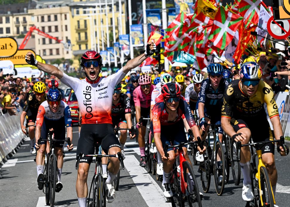 cyclist in white and red raises arms in celebration ahead of group