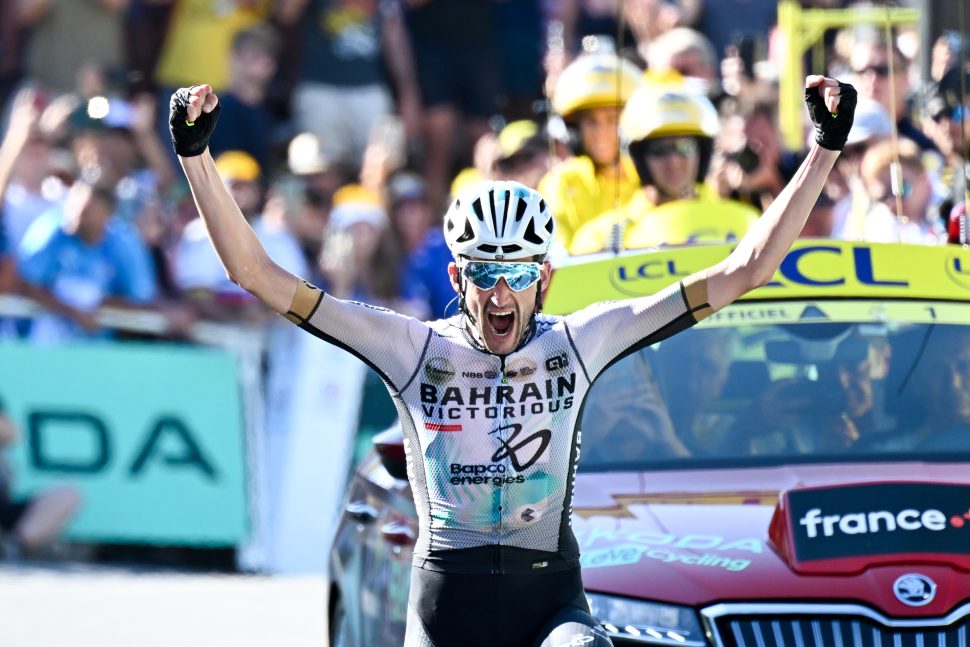 cyclist raises arms in air in celebration with mouth open